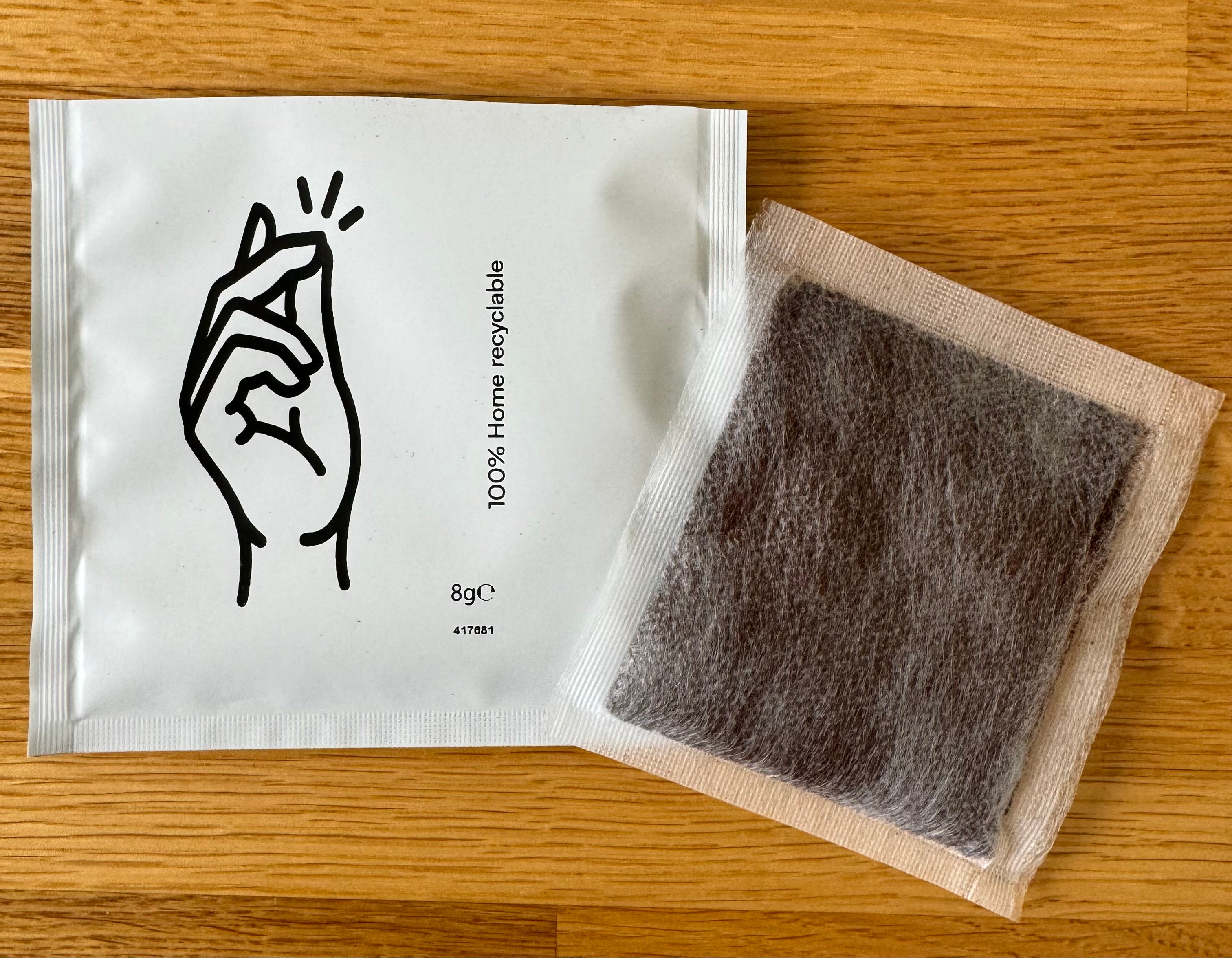 Home recyclable packaging bag with hand illustration and an opened tea bag on wooden surface.
