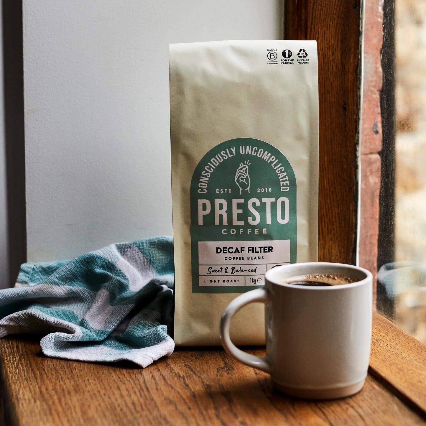 Presto Coffee Decaf Filter Beans, conscious coffee packaging, light roast label, cup of brewed coffee, cozy kitchen setting, eco-friendly recyclable packaging