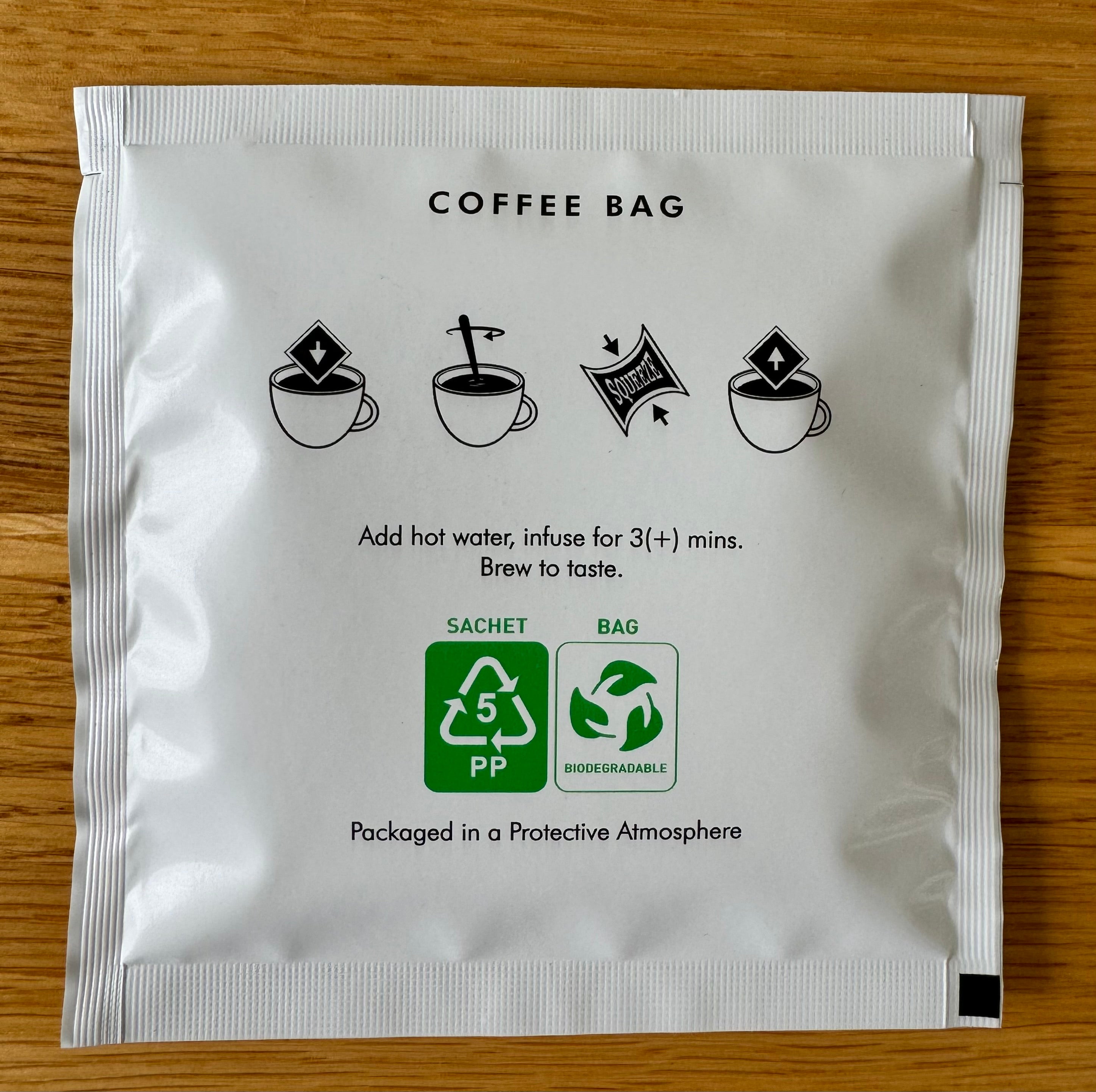 Coffee bag packaging with brewing instructions, eco-friendly symbols, recyclable sachet label, biodegradable bag icon, add hot water, brew for three minutes, protective atmosphere packaging, wooden surface background.