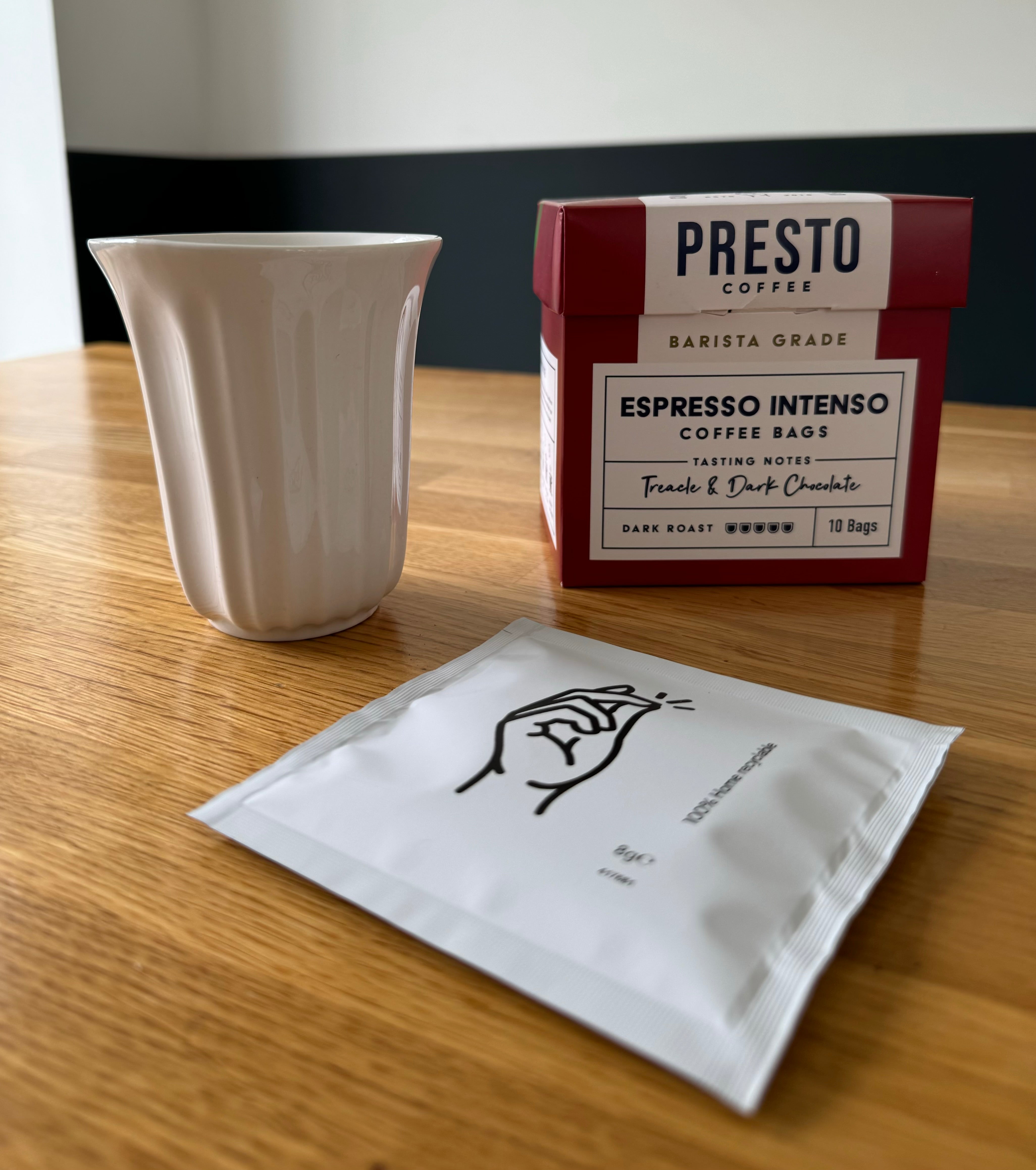 Espresso Intenso coffee bags by Presto on a wooden table with a white ceramic cup and an individual coffee bag.