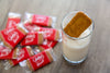 Glass of milkshake with a Lotus Biscoff cookie, surrounded by individually wrapped Lotus Biscoff biscuits on a wooden table.